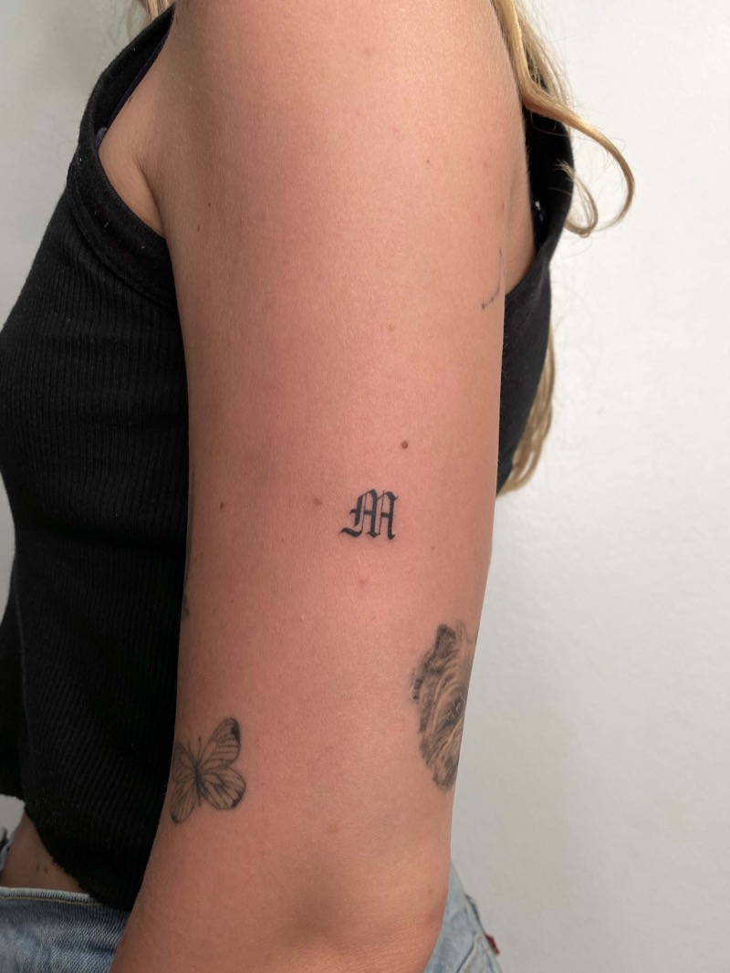 Gothic blackletter initial M tattoo on upper arm by Irka in Helsinki