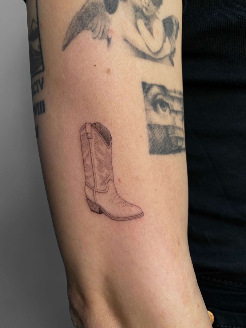Miniature cowboy boot tattoo on forearm by Irka in Helsinki